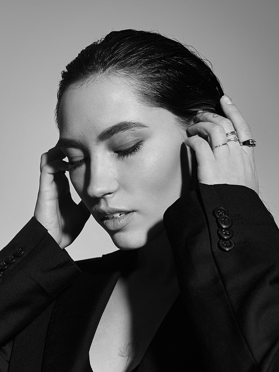 Woman in black suit, hands on head, contemplative.