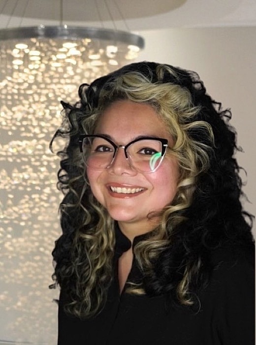 Smiling person with glasses and curly hair.